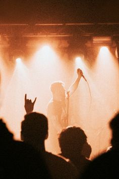 a person standing on stage with their hand up in the air and two microphones behind them