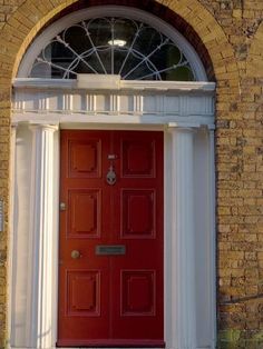 a red door is in front of a brick building with an arched window and white trim