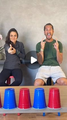 a man and woman sitting on top of a wooden table next to red, white and blue cones