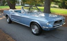 an old blue mustang is parked on the side of the road in front of some trees