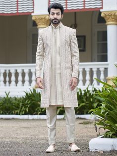 a man standing in front of a building wearing a white sherve coat and beige pants