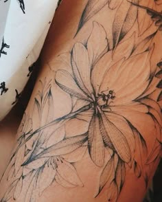 a woman's thigh with black and white tattoos on it, showing the flowers