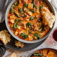 two pans filled with stew and bread on top of a table next to spoons