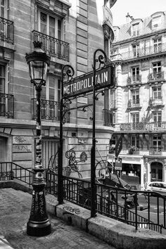 black and white photograph of metropolain street sign in paris, with cars parked on the side