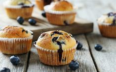 several blueberry muffins on a wooden table with fresh blueberries scattered around them