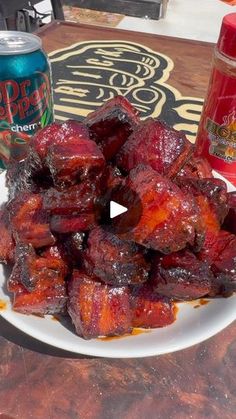 a white plate topped with meat next to a can of soda and a glass of beer