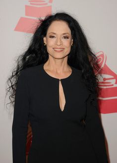 a woman with long black hair standing in front of a red and white wall wearing a black dress