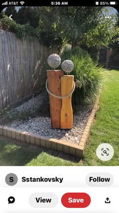 a wooden sculpture sitting in the middle of a garden next to a fence and grass