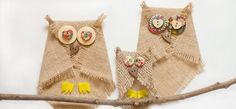 two burlap bags with owls on them hanging from a tree branch, one has buttons and the other has flowers