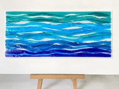 a painting is displayed on a easel in front of a white wall with blue and green waves