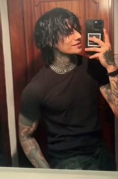 a man taking a selfie with his cell phone in front of him and tattoos on his arms