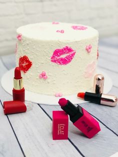 a white cake with pink and red lipstick on it next to two small bottles of lipstick