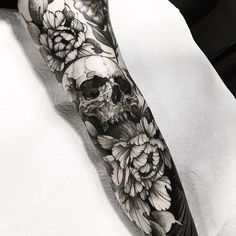 a black and white photo of a skull with flowers on it's forearm tattoo