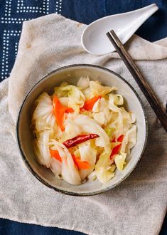 a bowl filled with cabbage and carrots next to chopsticks on top of a cloth