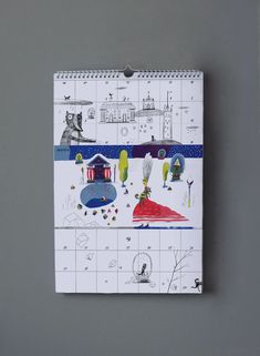 a calendar with drawings on it sitting on a table next to a gray wall,