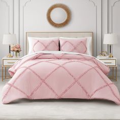 a bed with pink comforter and pillows in a white room next to a mirror