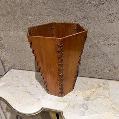 a wooden vase sitting on top of a white marble table next to a gray wall