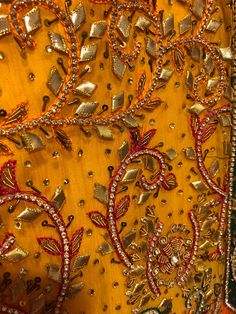 an embroidered yellow fabric with gold and red beads on it's edges, along with other beadings