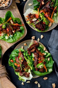 two plates filled with lettuce and meat on top of a wooden cutting board