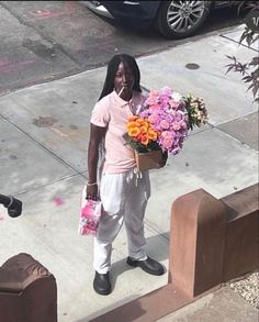 a woman standing on the sidewalk with flowers in her hand