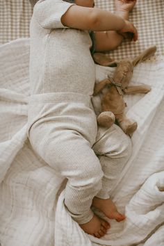 a baby laying on top of a bed next to a stuffed animal toy in his hand