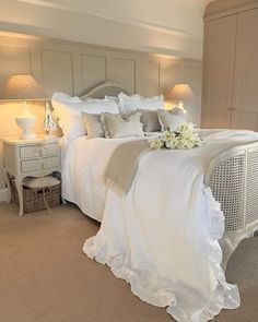 a white bed sitting in a bedroom next to two lamps and a table with flowers on it