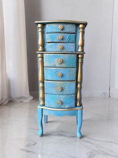 a blue dresser with gold handles and knobs on it's drawers in front of a window