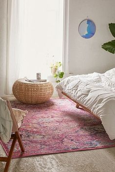 a room with a bed, chair and rug on the floor in front of a window