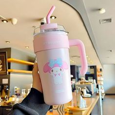 a person holding up a pink cup with a cartoon character on the side and a straw in it