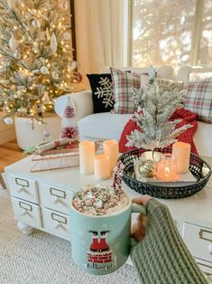 a person holding a coffee cup in front of a christmas tree with candles on it