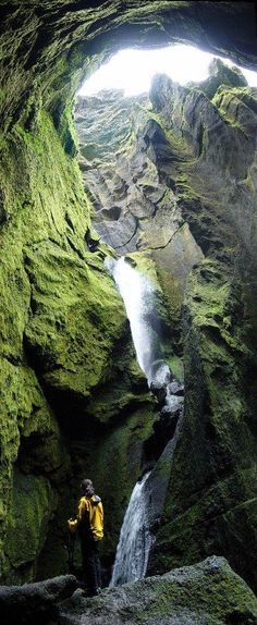 a man standing in the middle of a cave with a waterfall coming out of it