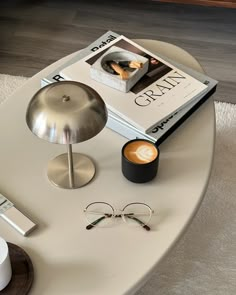 a coffee table with books, glasses and other items on it next to a lamp