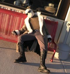 a man dressed in costume sitting on a bench next to a red metal bench and wearing black boots