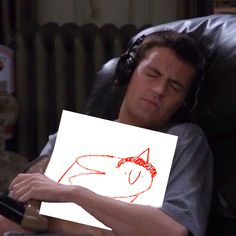 a man laying in a chair holding a piece of paper with a drawing of a cat on it