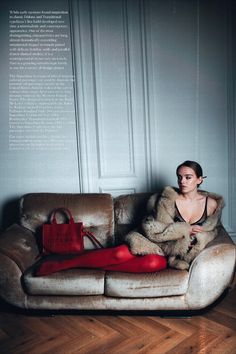 a woman sitting on top of a couch next to a red purse