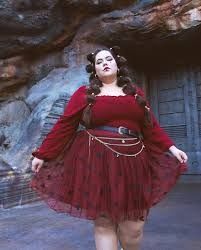 a woman in a red dress standing next to a rock formation with her hands on her hips