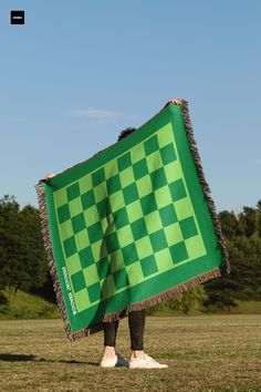 a person standing in a field holding a green and black checkered blanket over their head