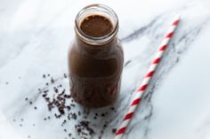 a glass jar filled with chocolate milk next to a striped straw on a marble surface