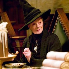 an older woman sitting at a table with food in front of her and wearing a witches hat