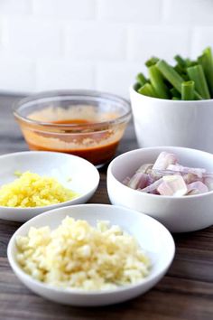 three white bowls filled with food sitting on top of a wooden table next to green onions