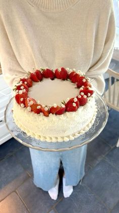 a person holding a cake with strawberries on it