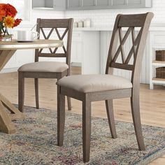 two wooden chairs sitting on top of a rug next to a table with flowers in it