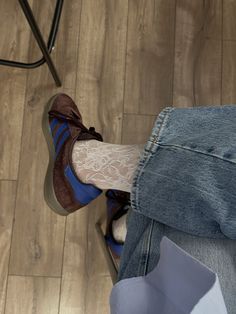 a person sitting on the floor with their legs crossed and wearing blue jeans, white socks and brown shoes