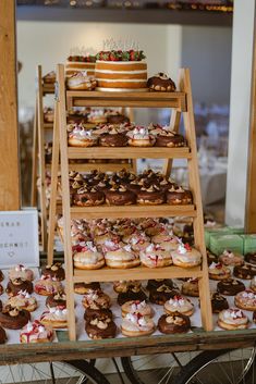 a table topped with lots of donuts covered in frosting next to a wooden ladder