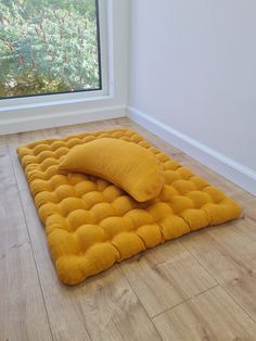 a large yellow pillow sitting on top of a wooden floor next to an open window