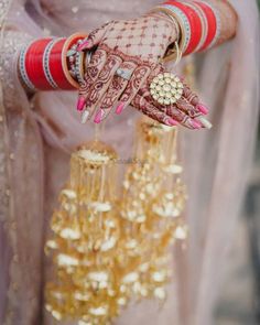 the bride is holding her hands with gold jewelry on their fingers and bracelets hanging from them