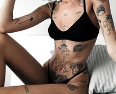 a woman with tattoos on her body sitting on a bed and posing for the camera