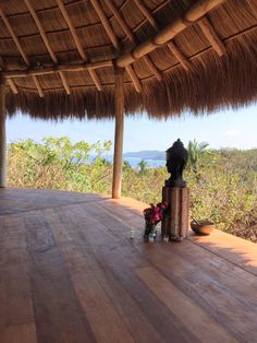 an outdoor area with wooden flooring and thatched roof over looking the ocean, surrounded by greenery