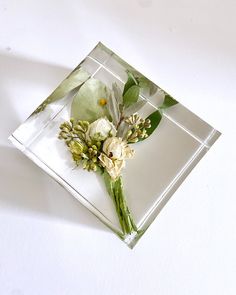 a flower is placed on top of a square glass block with leaves and flowers in it