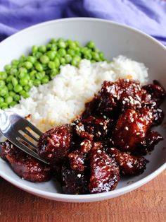 a white bowl filled with rice and meat next to green peas on a wooden table